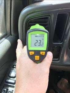A handheld thermometer measuring air temperature at a vehicle vent